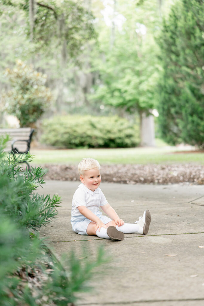 Toddler boy dressed in classic, Southern heirloom clothing sitting on the ground during family pictures in Savannah.