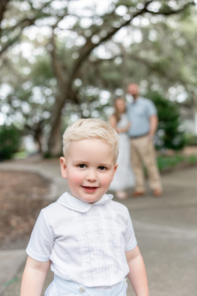 Little boy smiling while parents look on in the background during photography session with Tiffany Bradley Photography