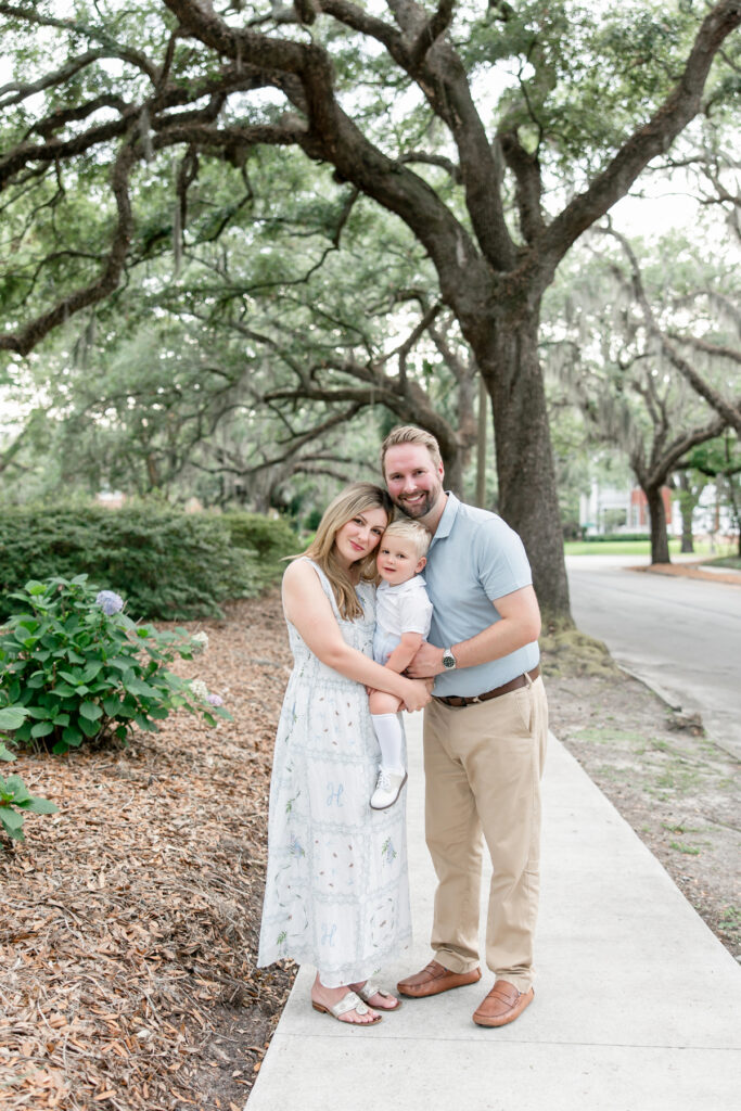 Family of three smiling under large oak trees with Spanish moss in Ardsley Park neighborhood
