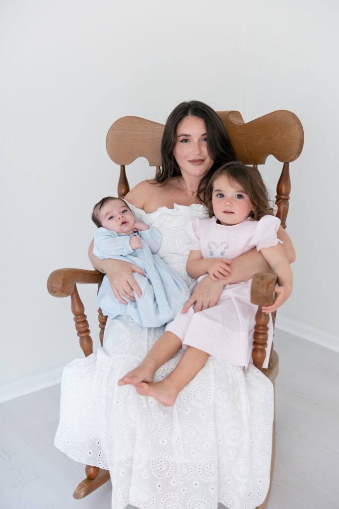 Mother cuddling her newborn baby and young daughter during their family portraits