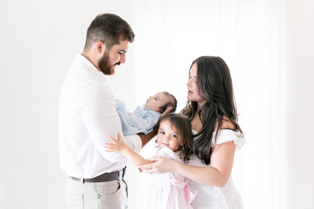 Parents and sibling interacting naturally with their newborn baby in the studio