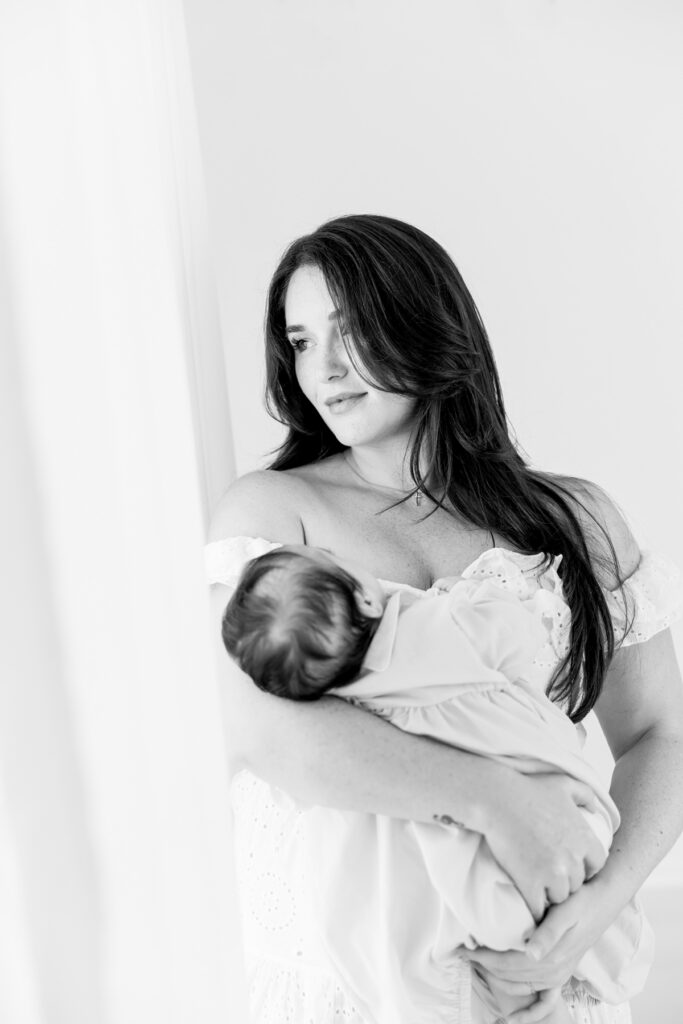 Black and white portrait of a mother holding her newborn baby in soft light from the studio window in Savannah, GA.
