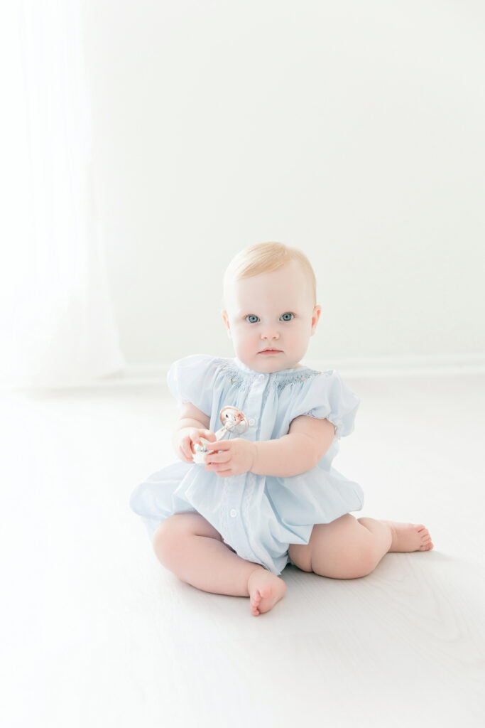 Baby girl holding a silver rattle during her first birthday portraits
