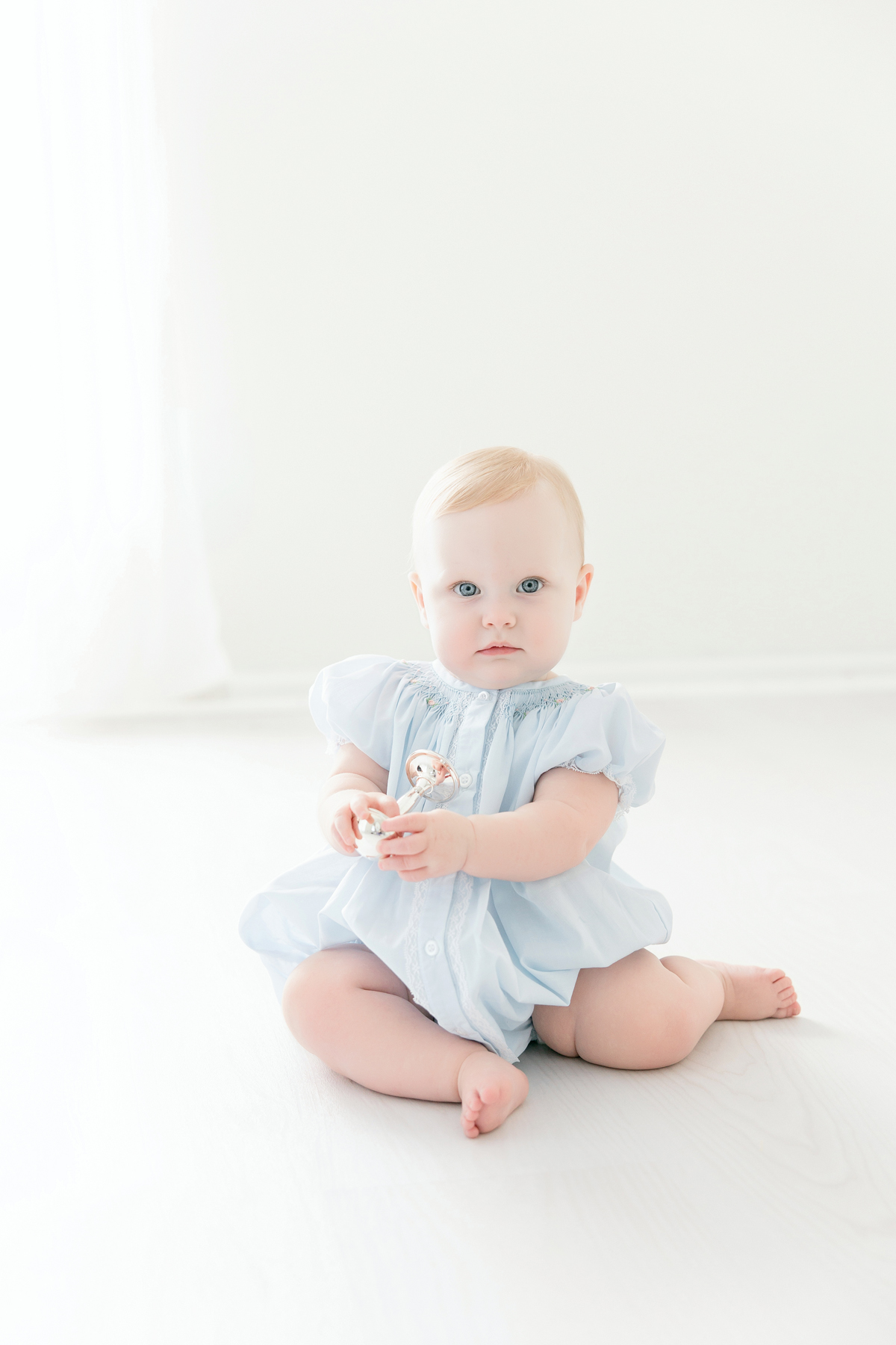 Baby girl holding a silver rattle during her first birthday portraits