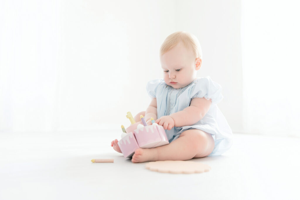 Baby girl playing with a wooden cake toy during her first birthday session
