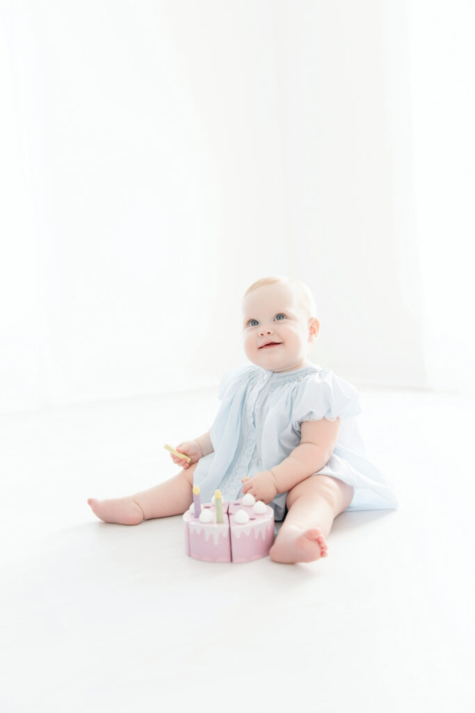 Baby girl wearing a blue bubble with lace and pink floral details at her first birthday session