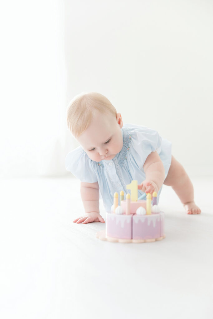 Baby girl playing with a wooden cake toy during her first birthday session