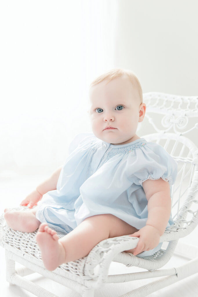 Baby girl sitting in white wicker chair during her first birthday portraits