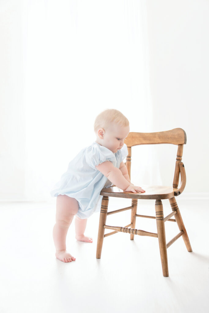 Baby girl holding on to wooden chair during 1st birthday session in Savannah