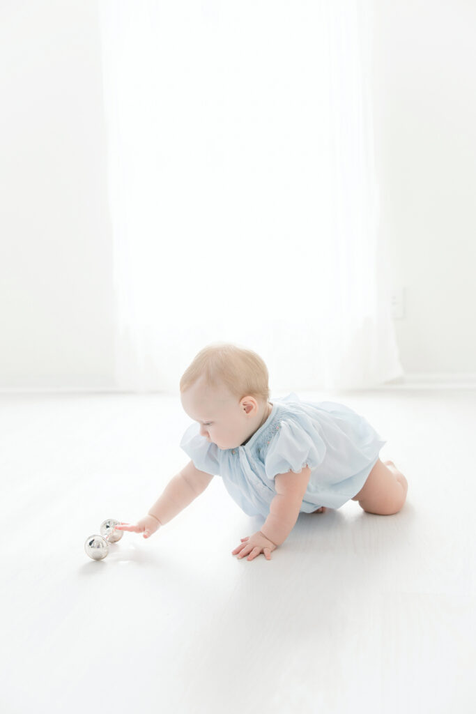 1 year old girl reaching for silver heirloom rattle during her first birthday portraits at Tiffany Bradley Photography's Savannah studio.